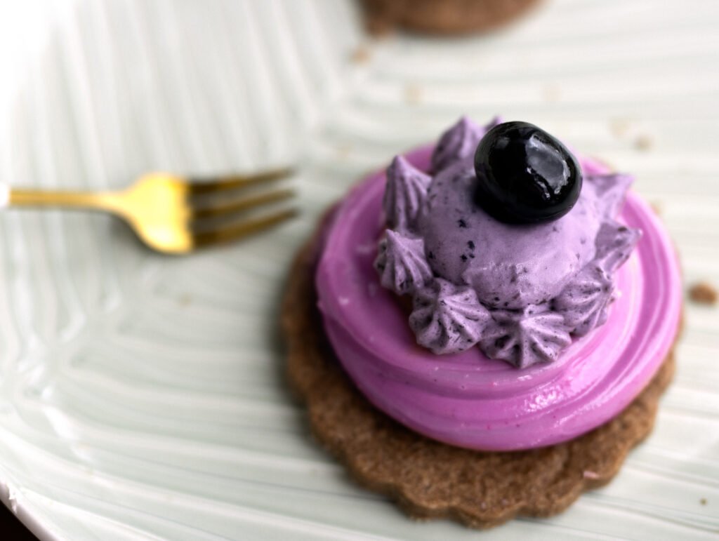 Törtchen mit violettem Heidelbeermousse-Topping und frischer Beere auf Mürbeteigboden